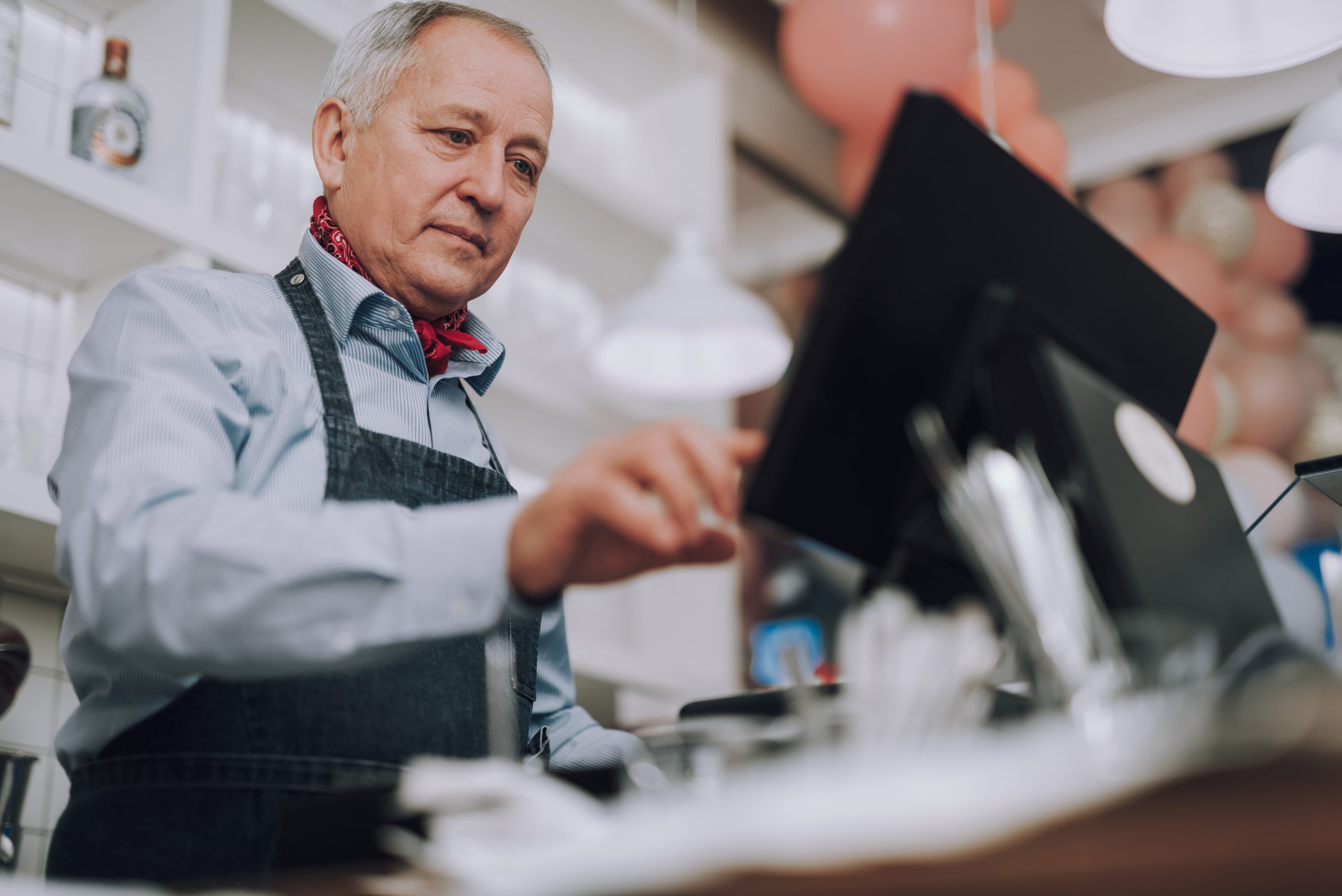 Senior man in denim apron working with digital cash register