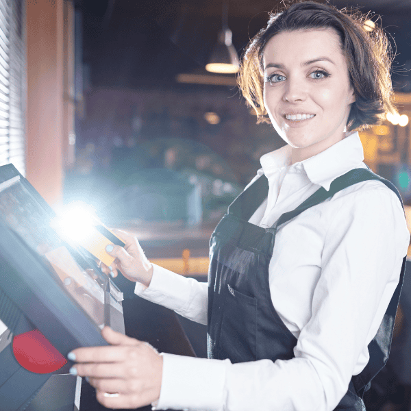 Restaurant waitress stood at a Restaurant EPOS terminal point looking at camera.